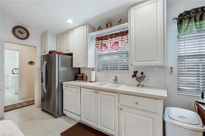 Kitchen with dishwasher, a sink, light tile patterned flooring, white cabinets, and light countertops