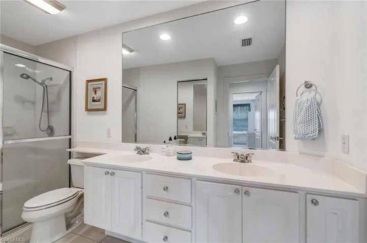 Bathroom featuring a stall shower, toilet, double vanity, recessed lighting, and tile patterned flooring
