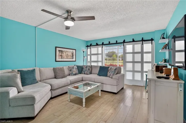 Living area featuring a barn door, light wood-type flooring, ceiling fan, and a textured ceiling