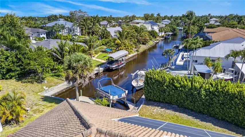Canal-front property featuring a private boat dock and lift, surrounded by mature tropical landscaping