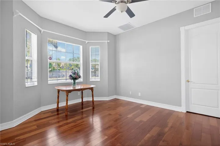 Bay window featuring multiple large windows, wood-finish flooring, light gray wall paint, a ceiling fan, and a white interior door