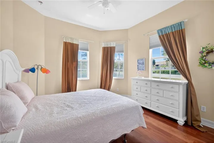 Bedroom featuring warm-toned walls, rich wood-finish flooring, multiple windows, and a ceiling fan