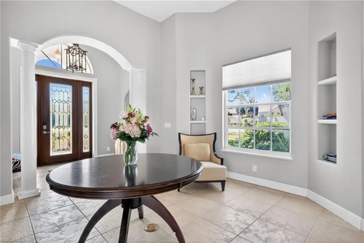 Foyer featuring high ceilings, arched architectural detailing, tile flooring, built-in wall niches, and a double-door entry with decorative glass inserts