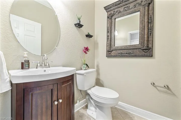 Bathroom with vanity, toilet, tile patterned floors, a textured wall, and baseboards