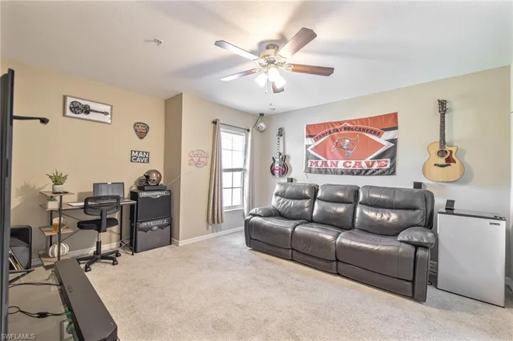 Carpeted living area featuring ceiling fan and baseboards