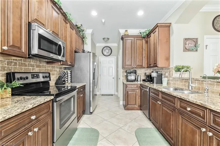 Kitchen featuring ornamental molding, light tile patterned floors, light stone countertops, appliances with stainless steel finishes, and a sink