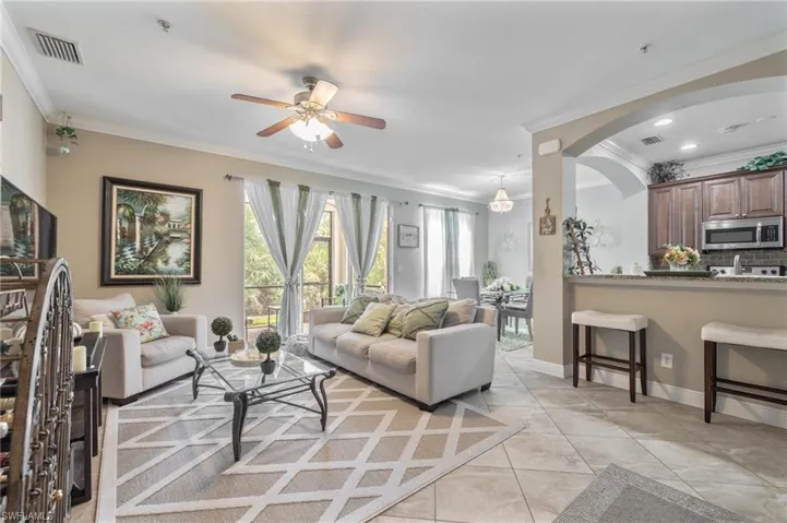 Living area featuring crown molding, ceiling fan, light tile patterned floors, arched walkways, and visible vents