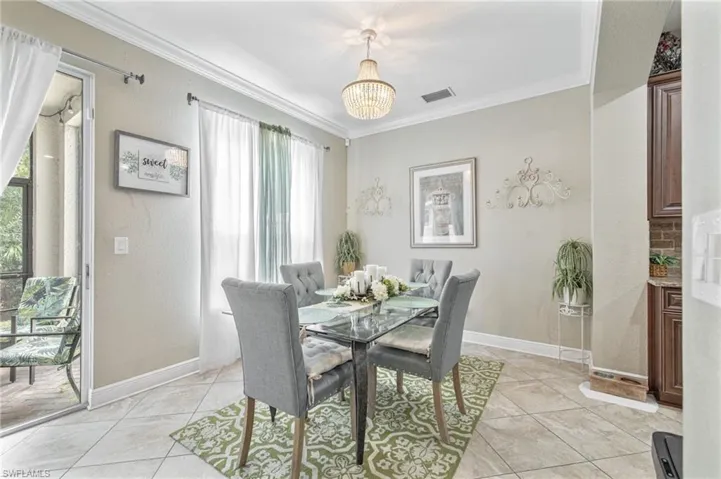 Dining area with light tile patterned floors, ornamental molding, visible vents, a chandelier, and baseboards