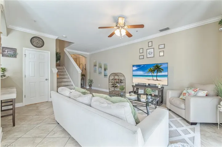 Living room featuring crown molding, visible vents, stairway, and a ceiling fan