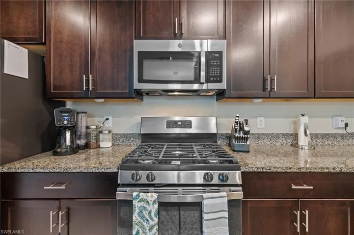 Kitchen featuring dark brown cabinetry, light stone countertops, and appliances with stainless steel finishes