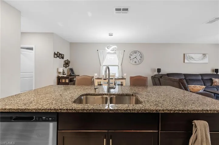 Kitchen featuring dark brown cabinets, light stone counters, stainless steel dishwasher, and sink