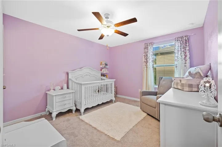 Bedroom with light colored carpet, a nursery area, and ceiling fan