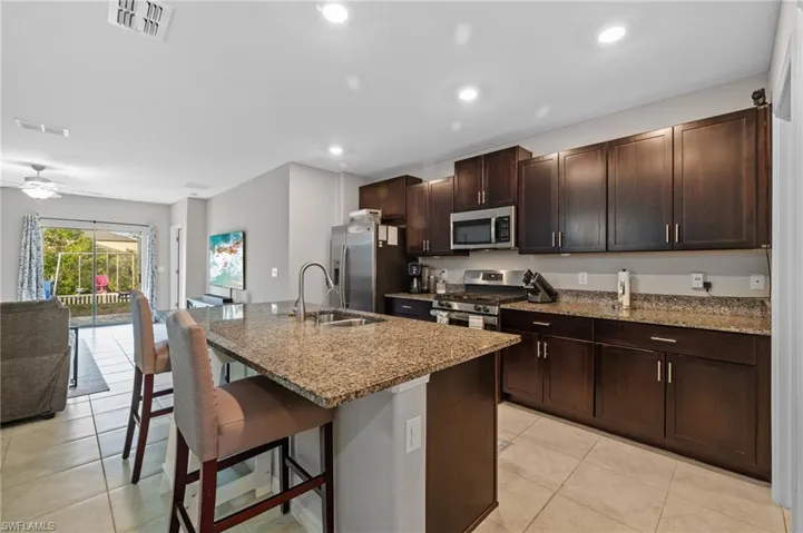 Kitchen with a breakfast bar, a kitchen island with sink, sink, ceiling fan, and stainless steel appliances