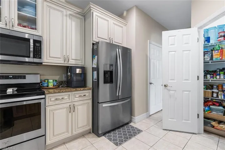 Kitchen with stainless steel appliances, light tile patterned floors, dark stone countertops, and cream cabinets