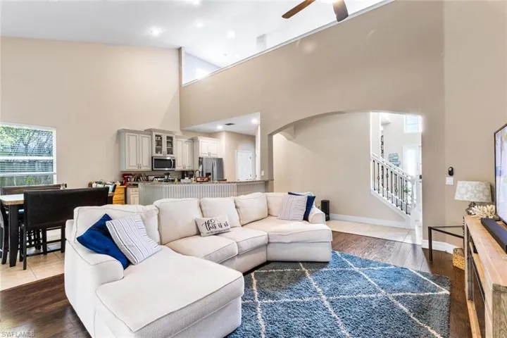 Living area with a towering ceiling, a ceiling fan, dark wood-style flooring, stairway, and arched walkways