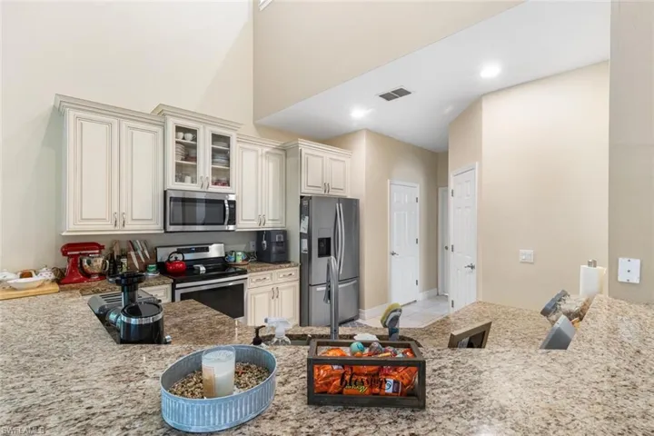 Kitchen with appliances with stainless steel finishes, light stone counters, glass insert cabinets, light tile patterned floors, and recessed lighting