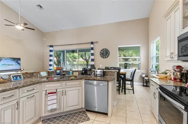 Kitchen with appliances with stainless steel finishes, a ceiling fan, light tile patterned floors, dark stone counters, and high vaulted ceiling