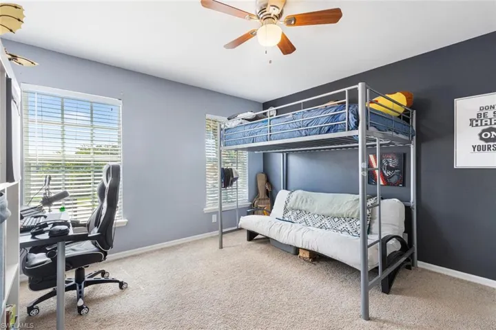Carpeted bedroom featuring an office area and a ceiling fan