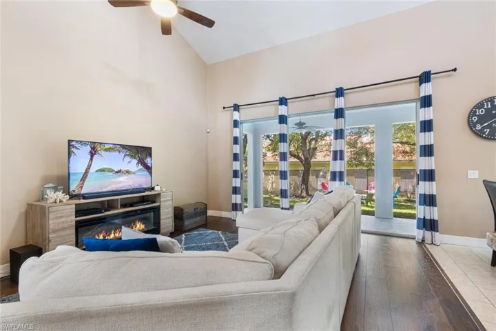 Living room featuring high vaulted ceiling, wood finished floors, ceiling fan, and a glass covered fireplace