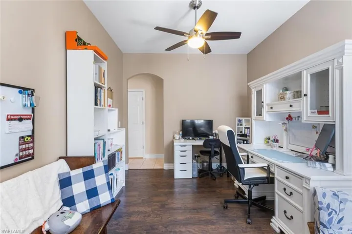 Office space with ceiling fan, arched walkways, and dark wood-type flooring
