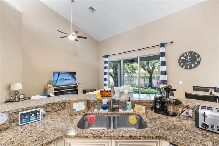 Kitchen featuring ceiling fan, open floor plan, light stone countertops, and high vaulted ceiling