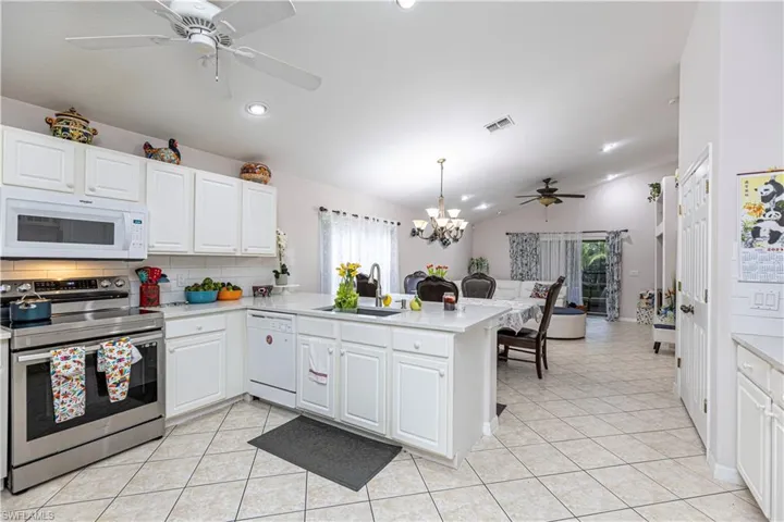 Kitchen featuring a wealth of natural light, kitchen peninsula, ceiling fan with notable chandelier, and white appliances