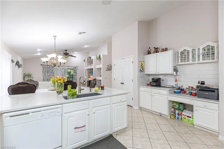 Kitchen featuring ceiling fan with notable chandelier, light tile patterned floors, sink, white dishwasher, and white cabinets