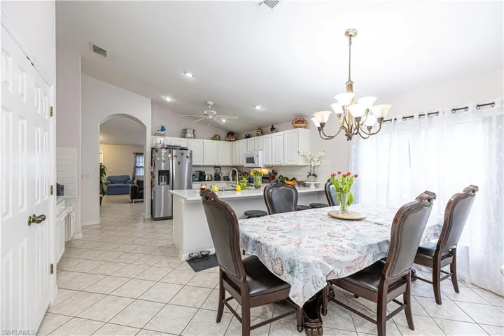 Dining area featuring ceiling fan with notable chandelier, vaulted ceiling, and light tile patterned floors