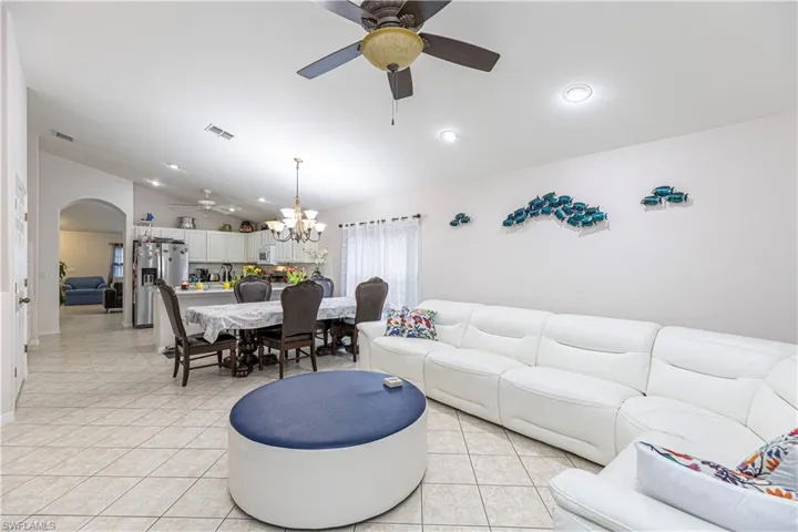 Living room with ceiling fan with notable chandelier, vaulted ceiling, and light tile patterned floors