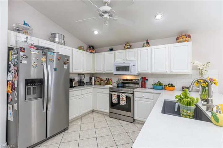 Kitchen featuring lofted ceiling, white cabinets, appliances with stainless steel finishes, and decorative backsplash