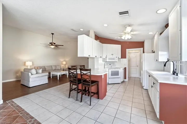 Kitchen featuring light tile patterned floors, white cabinetry, a breakfast bar, ceiling fan, and light countertops