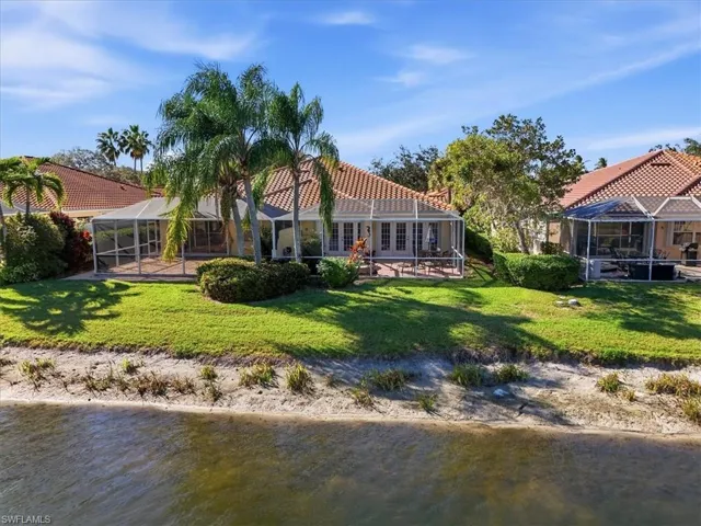 Back of property with a sunroom, glass enclosure, a water view, and a lawn