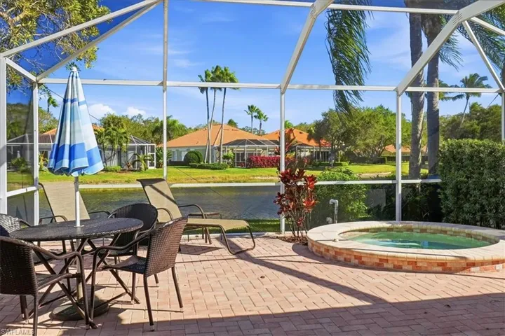 View of patio with an in-ground hot tub, a sunroom, glass enclosure, and a water view