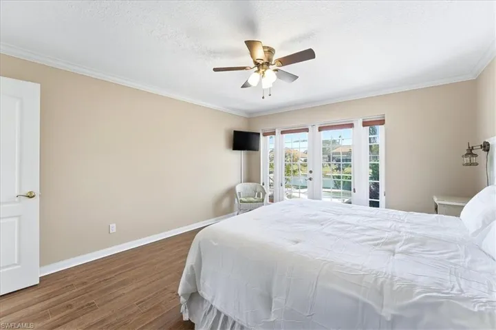 Bedroom featuring dark wood-style floors, access to exterior, a ceiling fan, crown molding, and french doors