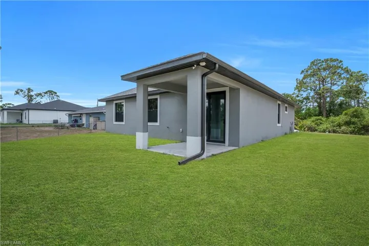 Rear exterior featuring a covered patio, stucco finish, and expansive lawn