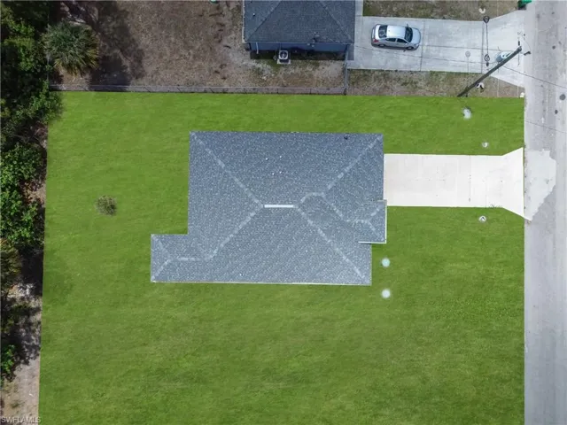 Expansive green lawn surrounds a single-story residence with a dark shingle roof and a concrete driveway