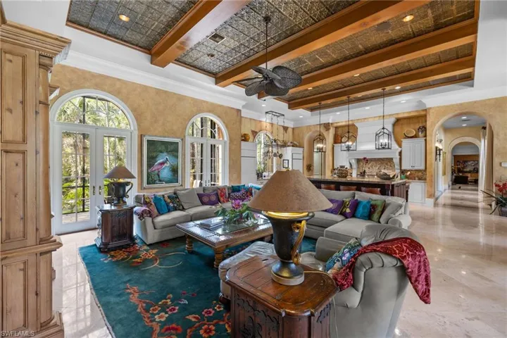 Spacious open-concept interior featuring a coffered ceiling with wood beams, arch-top French doors, stone tile flooring, a kitchen island with seating, and pendant lighting