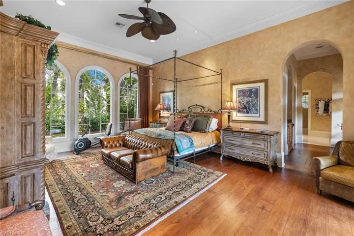 Hardwood flooring in a room featuring three arched windows, crown molding, an ornate ceiling fan, and arched doorways
