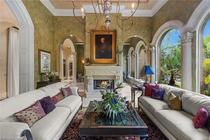 Living area featuring an ornate fireplace with a carved stone mantel, arched window openings with decorative columns, and a coffered ceiling with a chandelier