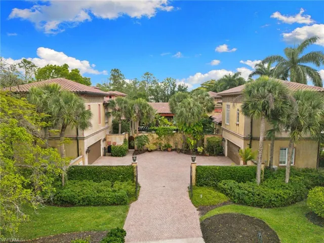 Mediterranean-style residence featuring a patterned paver driveway, terracotta roof tiles, stucco exterior, integrated garage doors, and lush tropical landscaping
