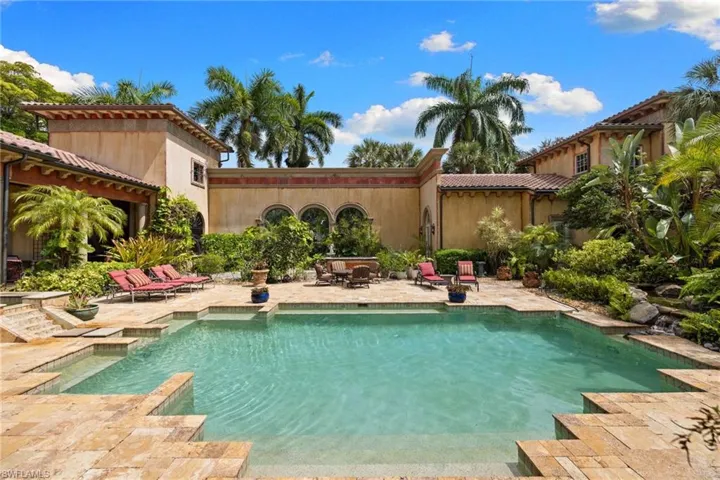 Expansive outdoor living area featuring a rectangular swimming pool with integrated steps, surrounded by stone paver decking