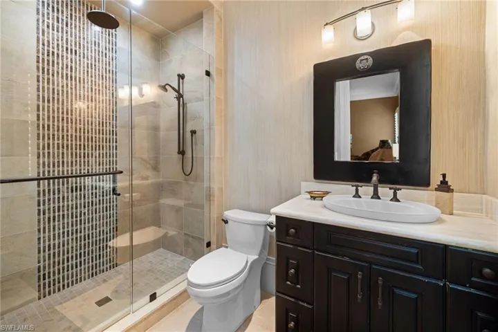 Walk-in shower with vertical mosaic tile accent, glass enclosure, built-in bench, and a rain showerhead