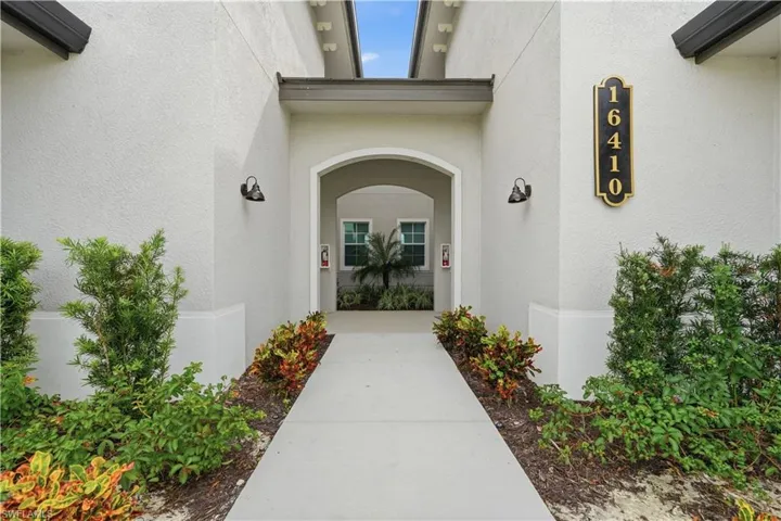 Archway entryway with textured stucco exterior, dual wall-mounted lighting, and a well-defined address plaque