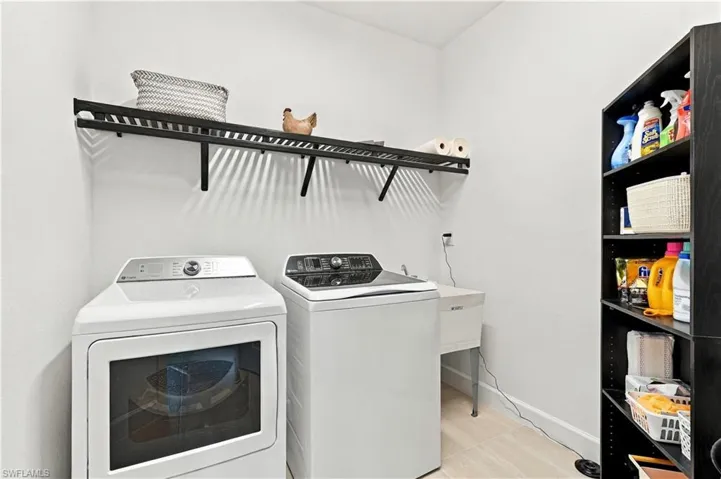 Laundry area with light-toned flooring, wall-mounted shelving, built-in utility sink, and tall storage unit