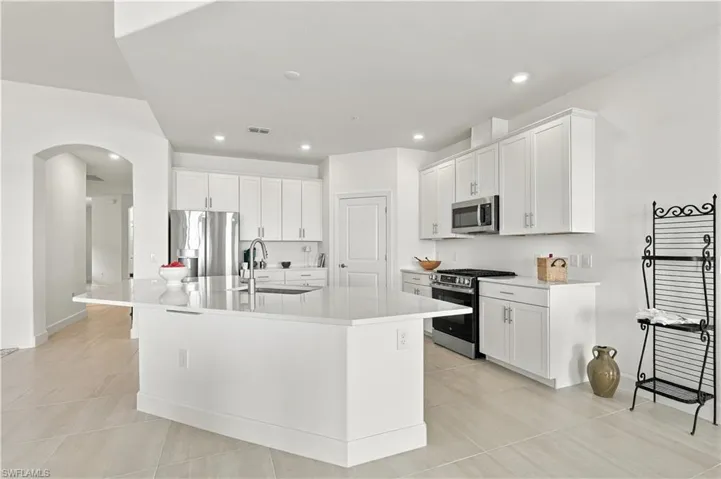 Spacious kitchen featuring an expansive central island, stainless steel appliances, white cabinetry with silver-tone hardware, recessed lighting, and large format floor tiling