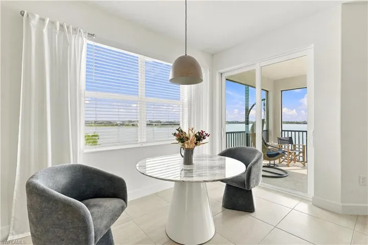 Tiled flooring throughout, large window with horizontal blinds, sliding glass door leading to a balcony, and a pendant light fixture