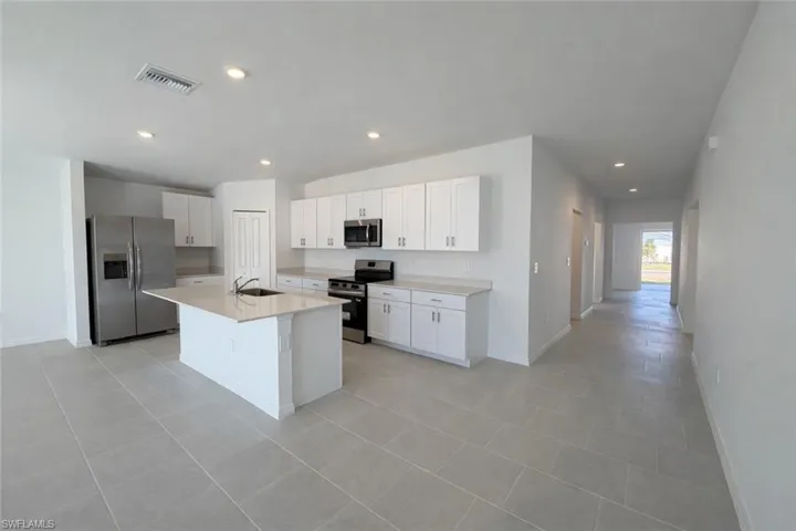 Kitchen with stainless steel appliances, white cabinetry, recessed lighting, an island with sink, and light tile patterned floors