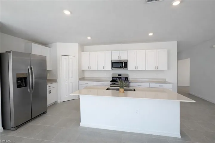 Kitchen featuring stainless steel appliances, white cabinets, light stone counters, an island with sink, and recessed lighting