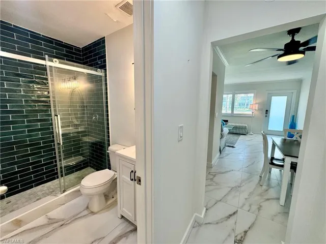 Bathroom featuring ceiling fan, a shower with shower door, tile floors, toilet, and vanity