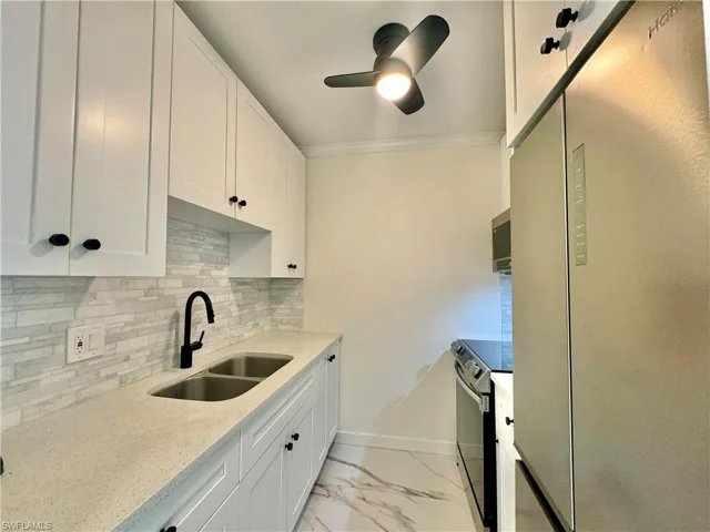 Kitchen featuring light tile flooring, backsplash, sink, white cabinetry, and appliances with stainless steel finishes